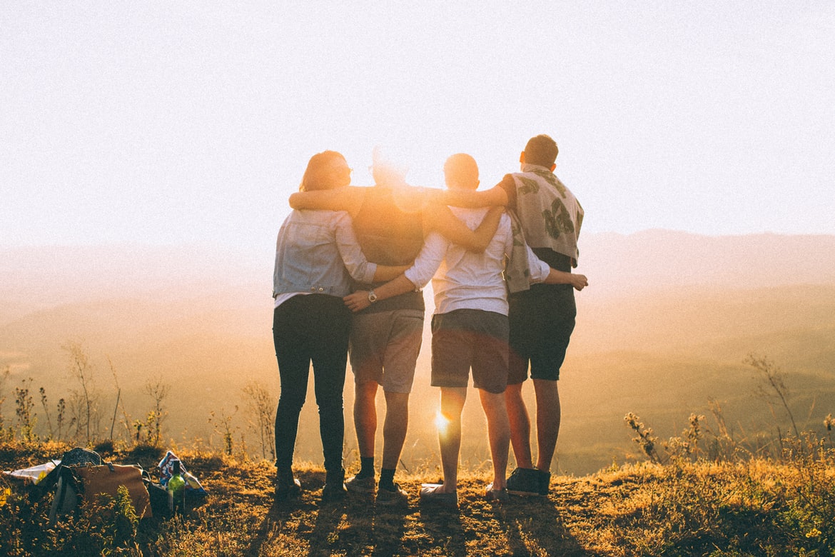 Four people with arms around each other looking at the sunset
